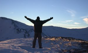 Image of a man standing on snowy mountain top with arms stretch towards sky