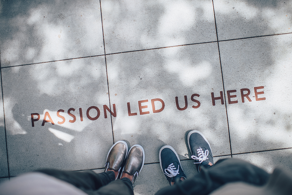 Image of two sets of feet looking down at sidewalk engraved with "Passion led us here"